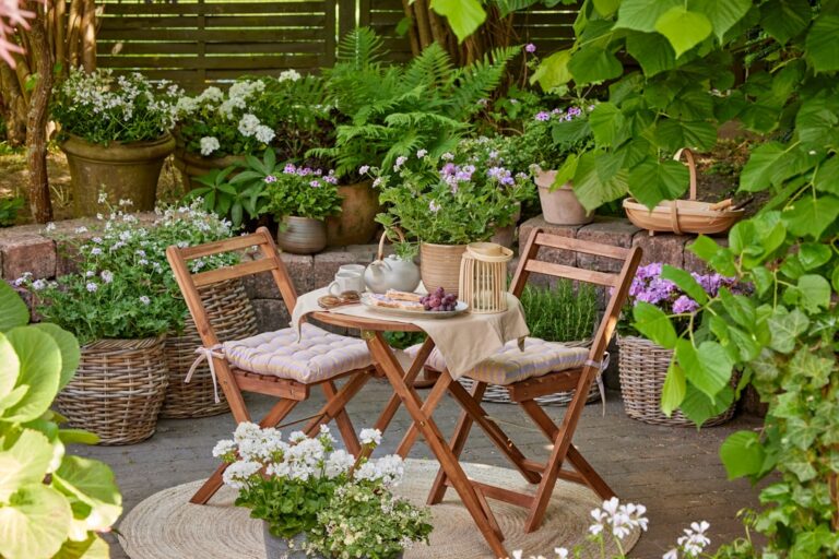 Two people relaxing on a small patio with compact furniture, potted plants, and string lights in the evening.