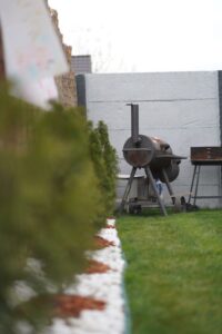 A person assembles a wooden raised garden bed in a sunny backyard with grass and shrubs nearby.