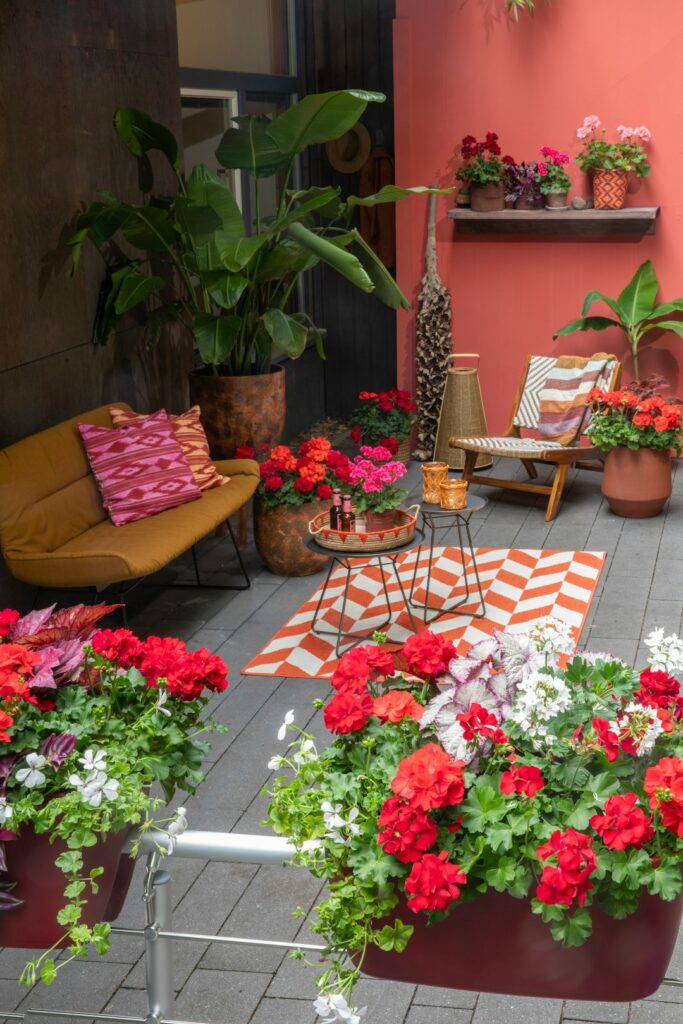 A shaded patio with coordinated cushions, planters, green foliage, and warm neutral paving.