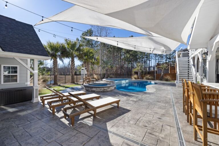 People relaxing on a shaded patio with fans and light-colored furniture on a sunny afternoon.