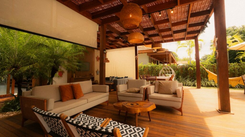 A flatweave outdoor rug anchors lounge furniture on a covered patio beside potted plants.